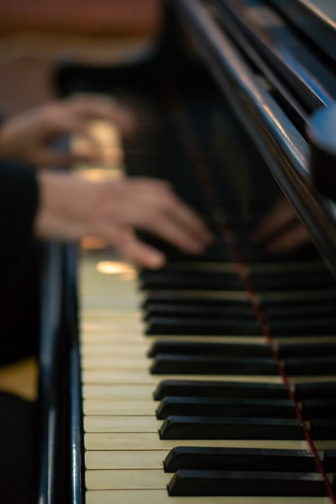 close-up of a piano keyboard- shiny, grand piano with aged keys. hands playing with a slight blur